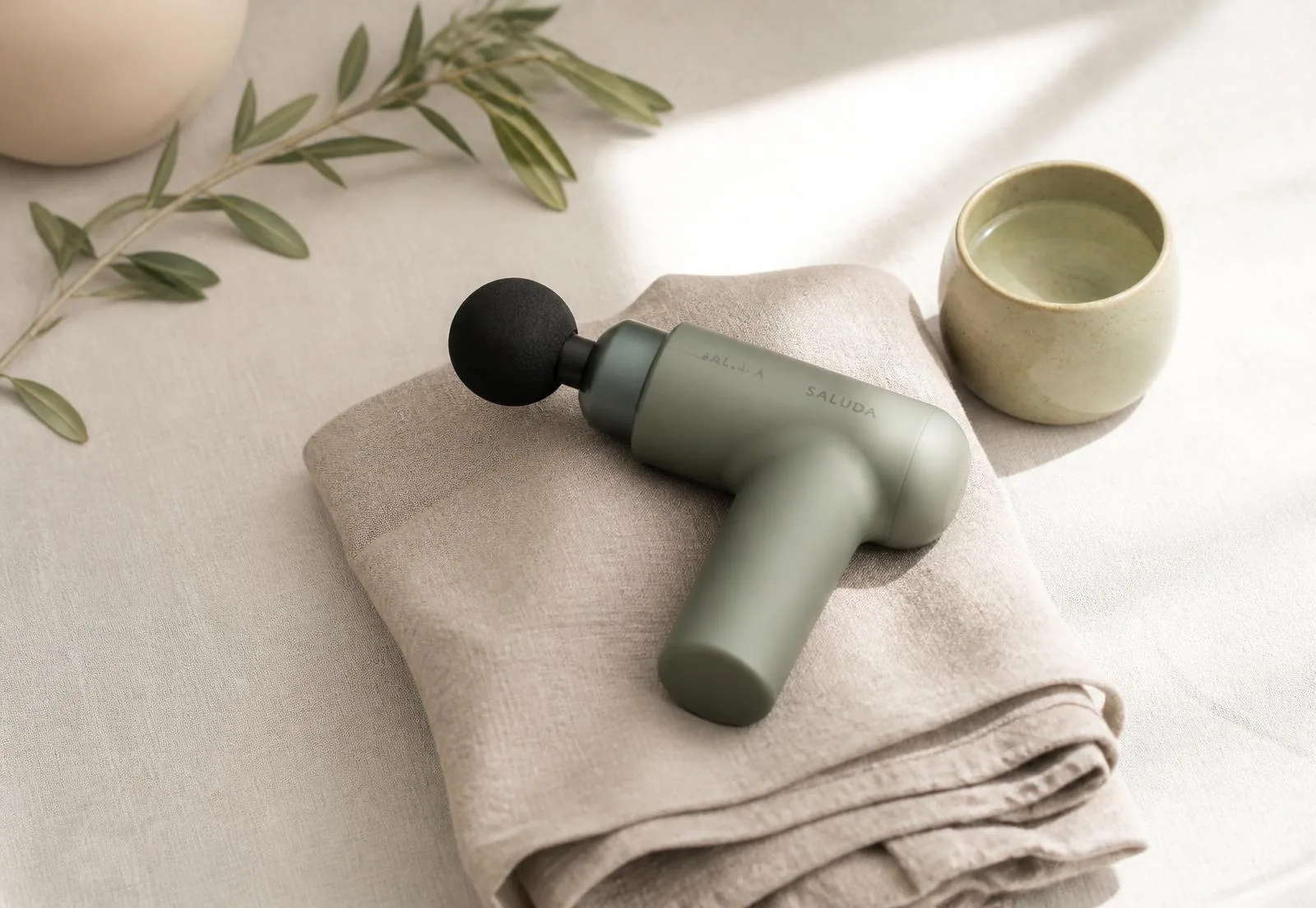 Pistolet de massage posé sur un linge de lin dans une lumière douce