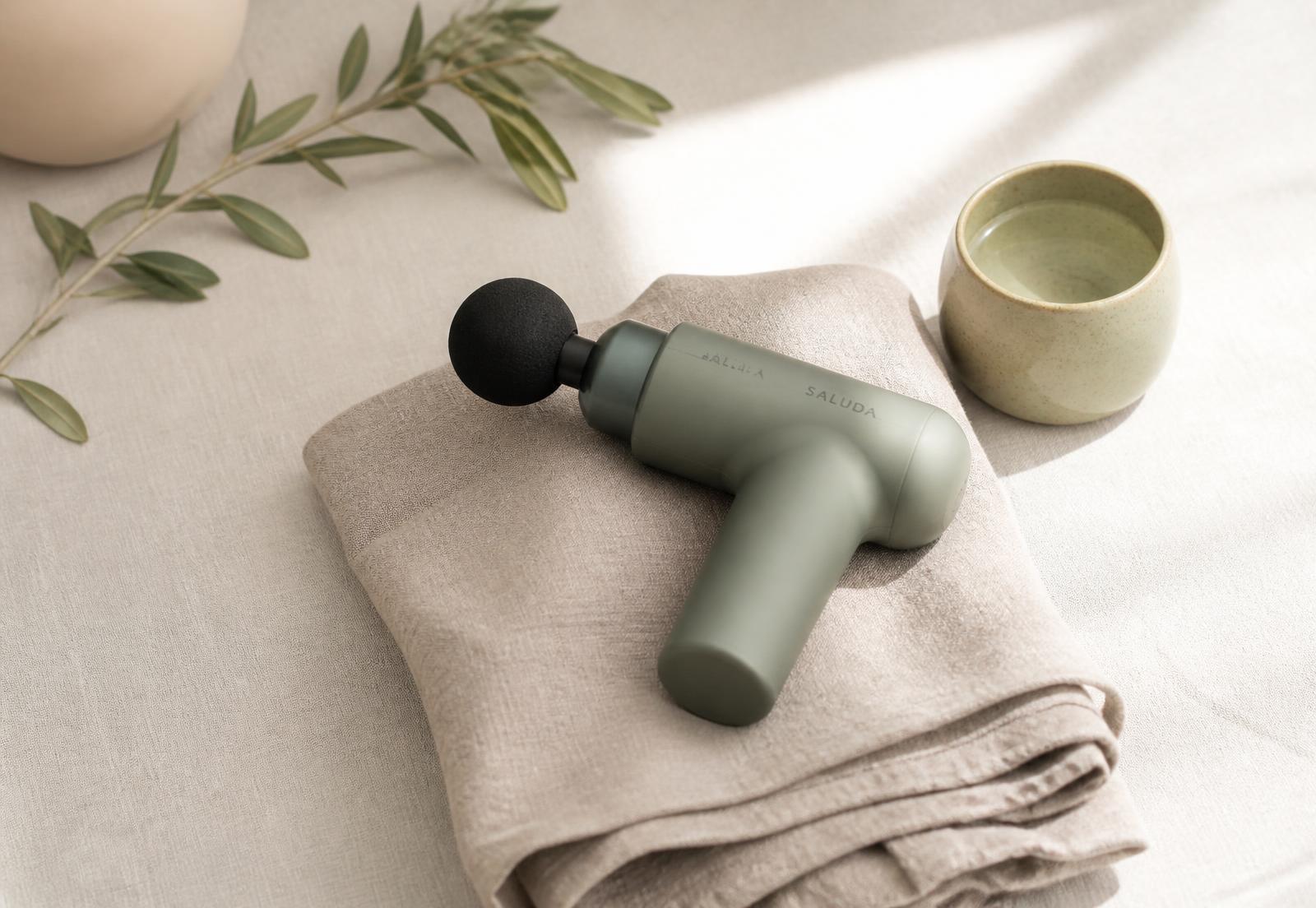 Pistolet de massage posé sur un linge de lin dans une lumière douce